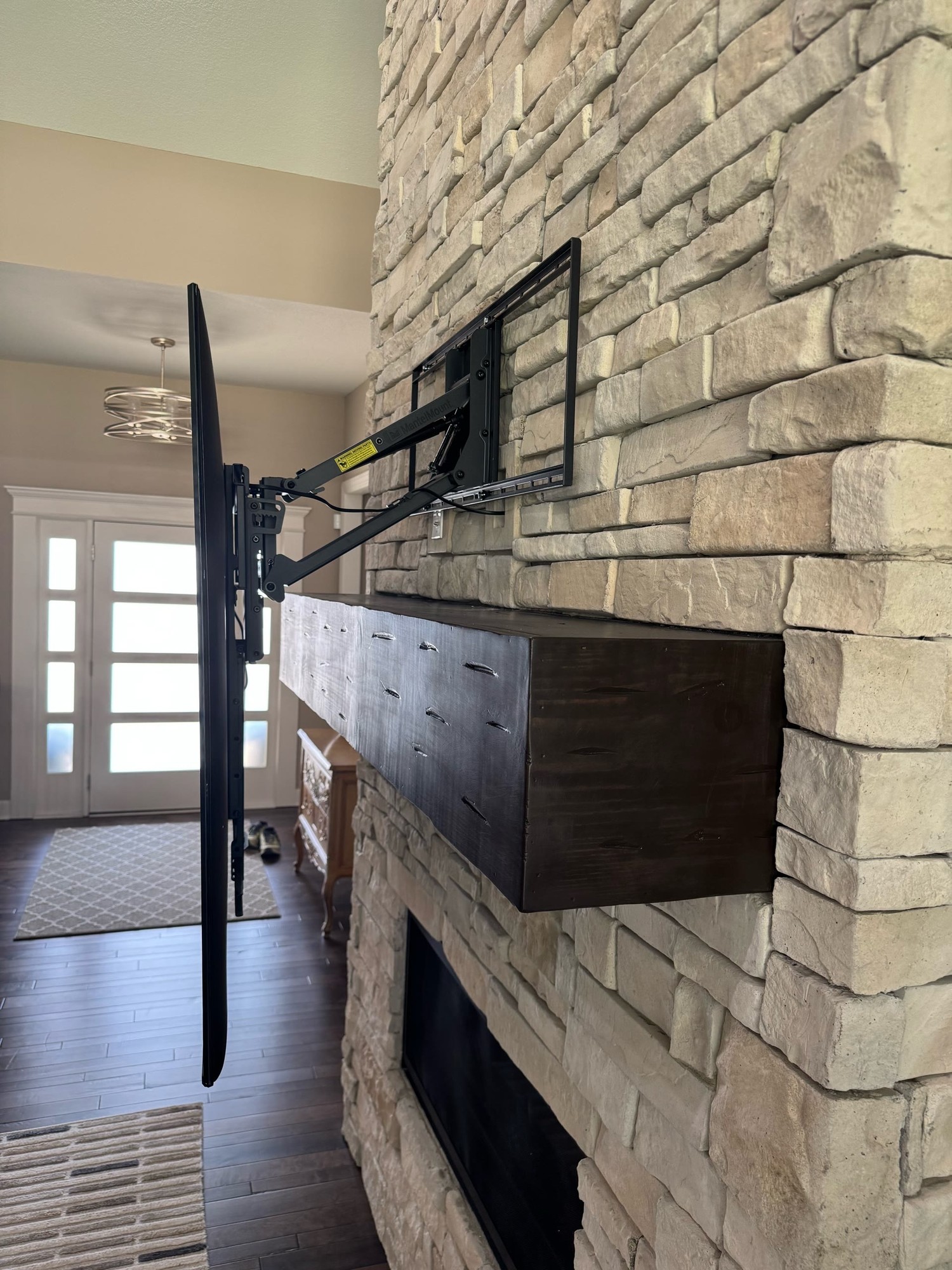 MantelMount side view with TV pulled down to eye level over a stone fireplace, clean wiring along the mount arm