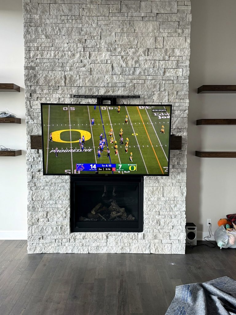 Football game on a wall-mounted TV above a stone fireplace in a Kansas City living room, installed by SmartHome Connect